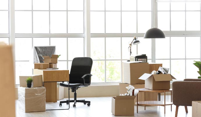 Office interior with moving boxes, empty desk, and black chair beside large windows