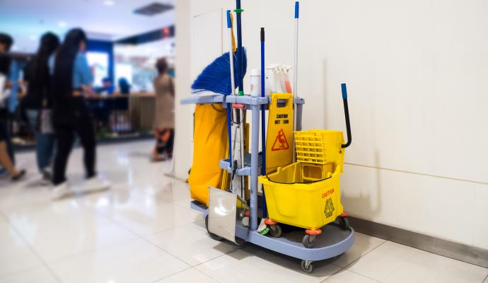 Cleaning cart loaded with maintenance tools and supplies placed near pedestrian walkway in commercial building