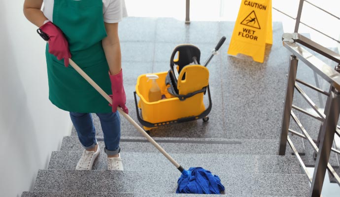 Worker cleaning stair with mop wearing protective gloves and apron