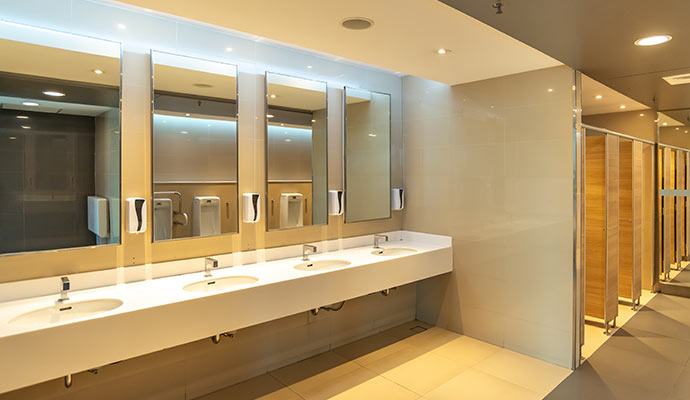 A bright, modern commercial restroom with a long white vanity, multiple sinks, mirrors, and clean tile floors