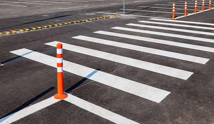A newly painted white crosswalk and bright orange safety bollards on a clean asphalt parking lot