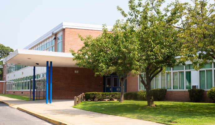 Neatly maintained school building with brick exterior, large windows, landscaped greenery, and a clean entrance area