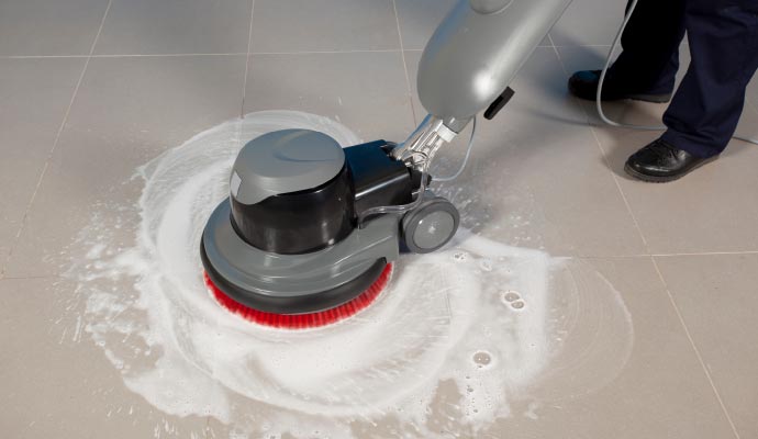 A person cleaning tile floor using floor scrubber
