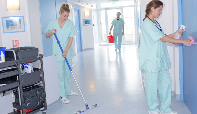 Cleaning staff mopping and wiping surfaces in a medical hallway