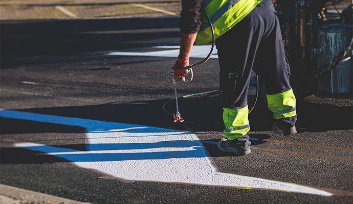 Worker paints a crisp directional arrow on a parking lot surface