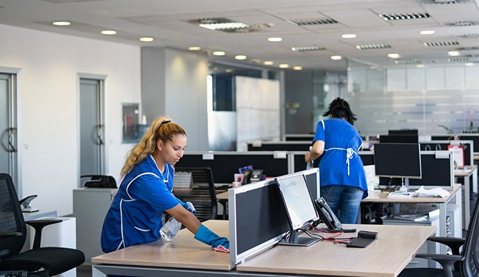 Multiple cleaners sanitizing workstations in a large facility.