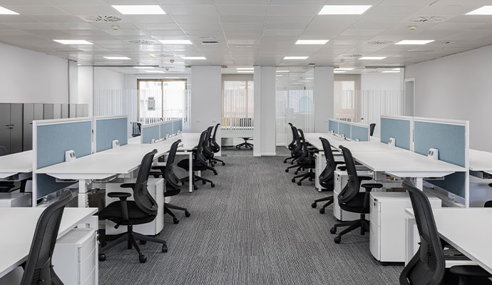 A wide view of a bright, perfectly cleaned modern office with white desks and black chairs.
