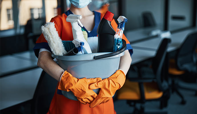 Person holding bucket of spray bottles, brush, and bottles