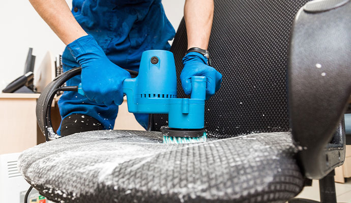 A cleaner using a power brush to deep clean an office chair.