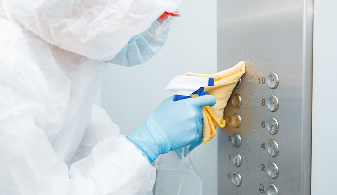 A cleaner in a hazmat suit sanitizing elevator buttons.