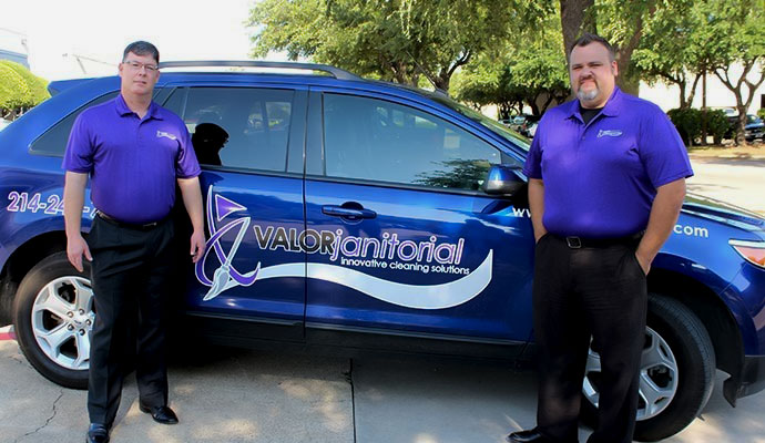 Two technicians in purple shirts standing by a company car.